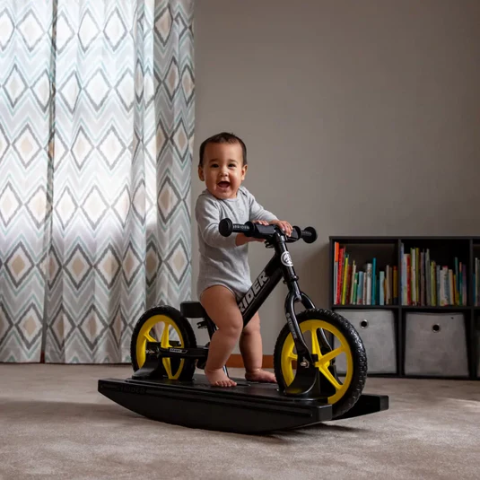 A toddler have a wide bright smile on his face riding a strider 2 in 1 rocking bike. Best sensory gift for ADHD babies and toddlers.